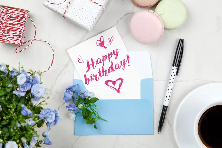 Celebratory birthday setup with a card, flowers, and coffee on a desk.