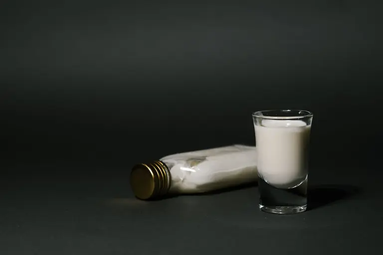 A minimalist still life photo featuring a milk bottle and a shot glass on a black surface.